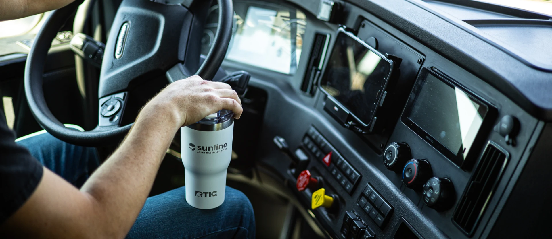 Driver holiding a Sunline branded tumbler on his knee in the truck cab