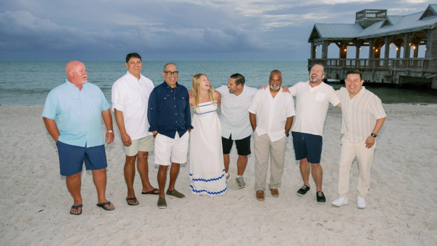Group of Sunline employees laughing and posing together on a beach at sunset